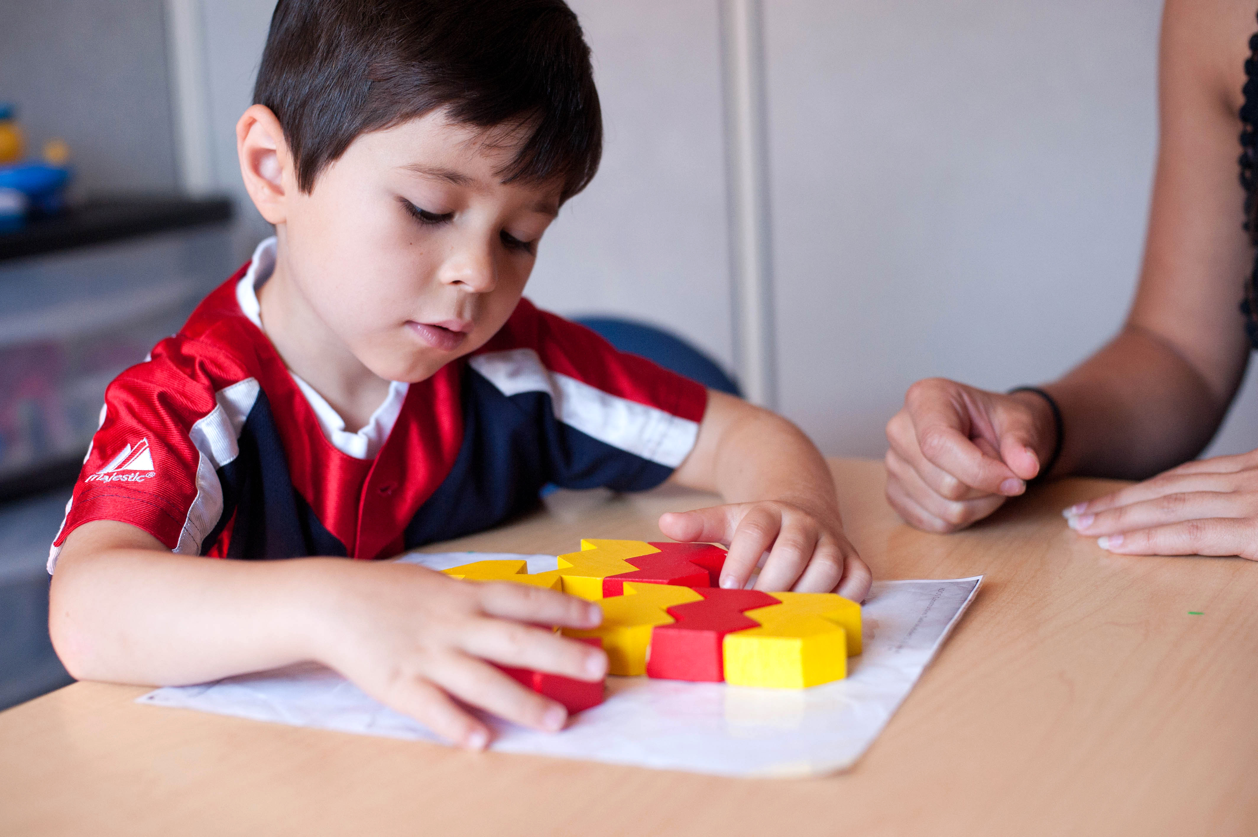 A child with dark hair plays with yellow and red squares at a table.