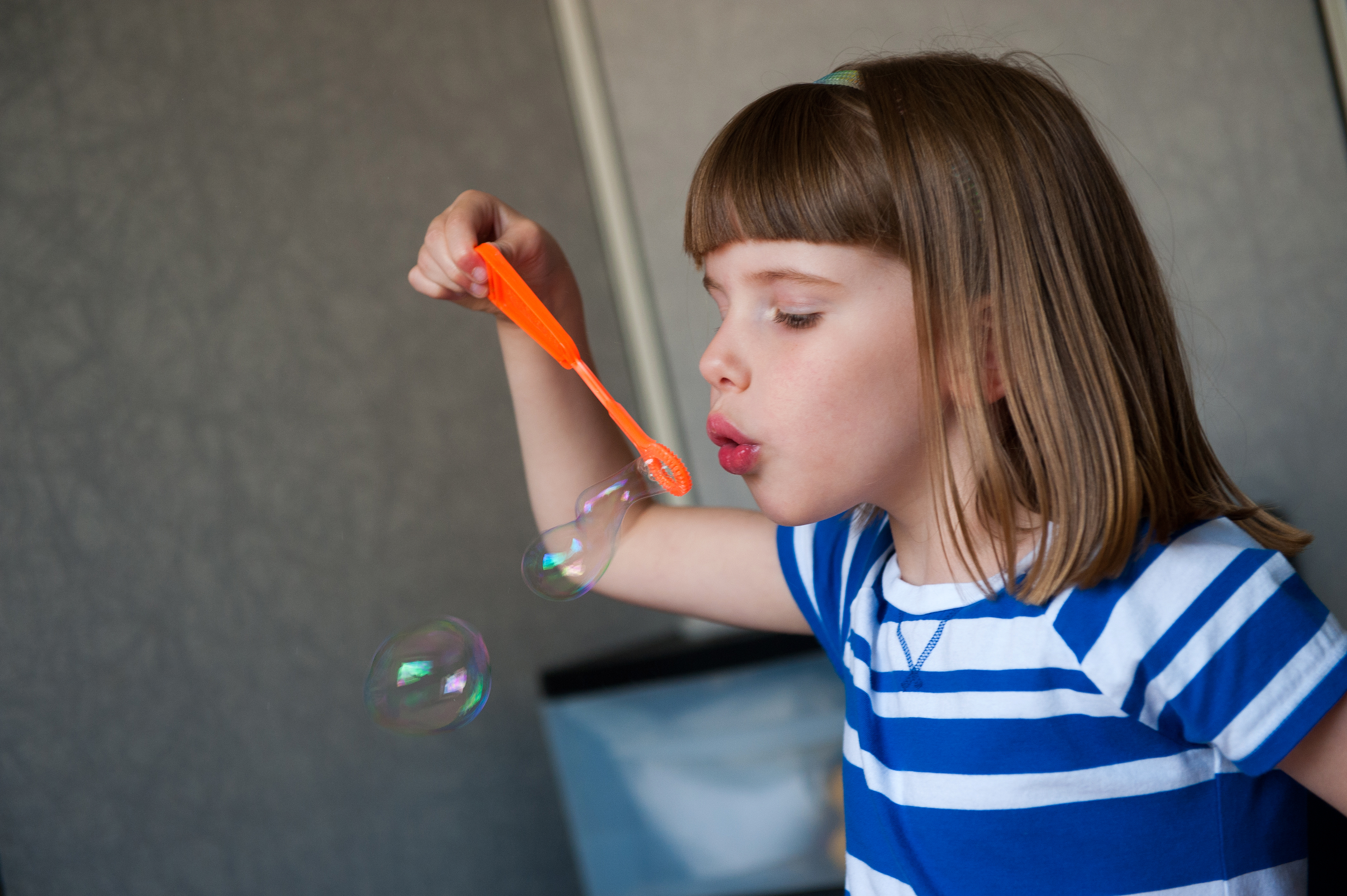 A little girl blows bubbles with an orange bubble wand.