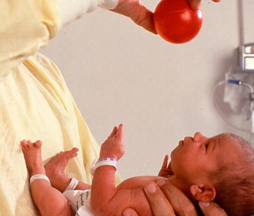 A doctor holds a small red ball over a newborn baby. 
