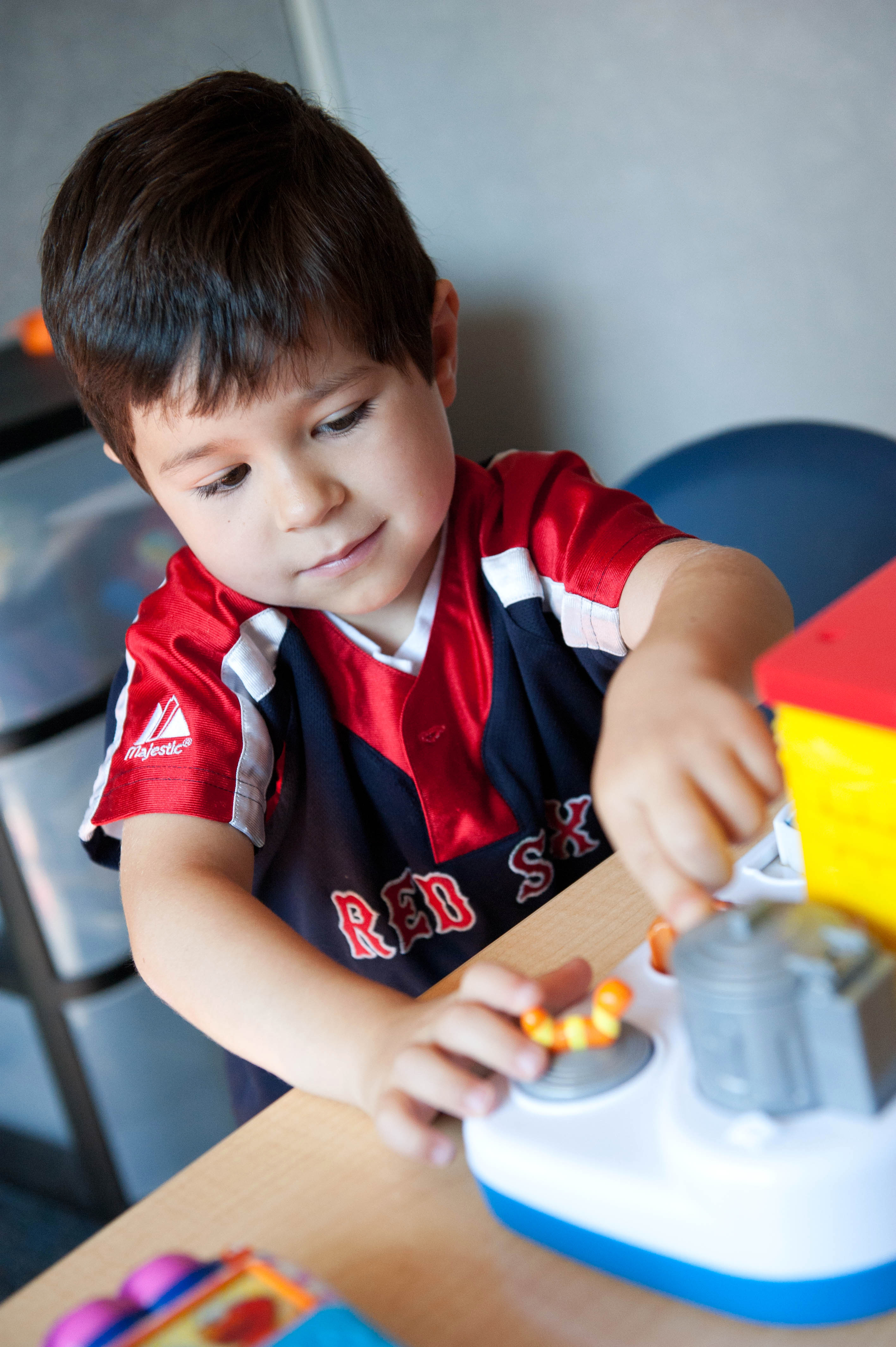 young, dark-haired boy in Red Sox jersey sits at a wood table and plays with toys