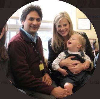 An image of a dark-haired dad and a blonde mom holding a laughing baby.