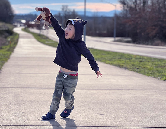 Young boy walks down wide sidewalk holding a stuffed animal in his right hand.