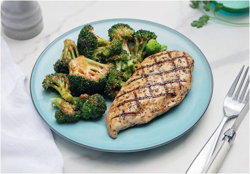 A plate of grilled hickory chicken and a side of broccoli on a blue plate. 