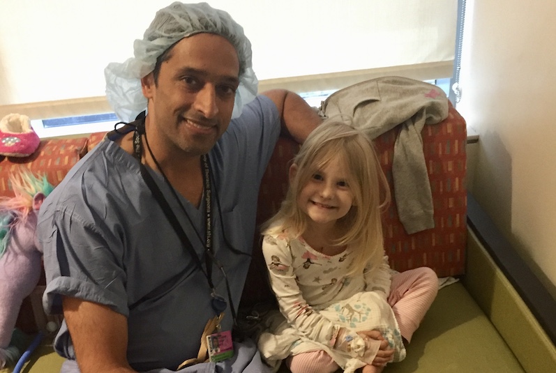 Doctor and young girl pose together in hospital room.