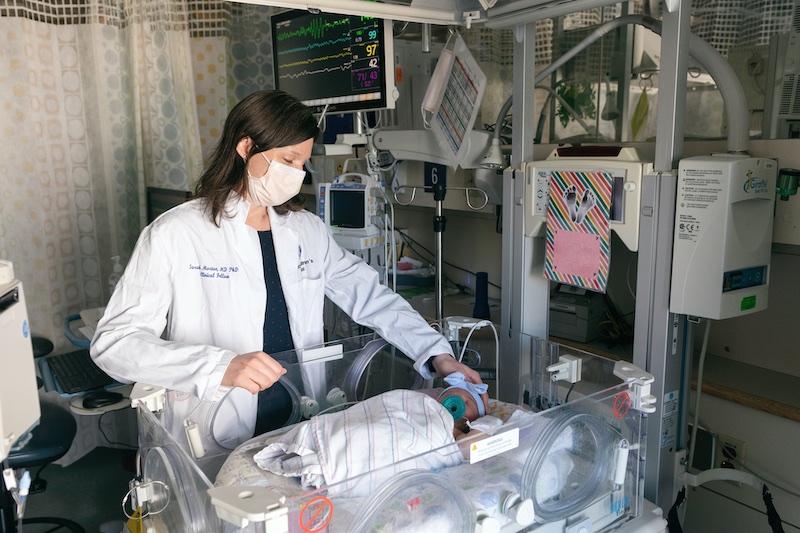 Female doctor checks on baby in incubator