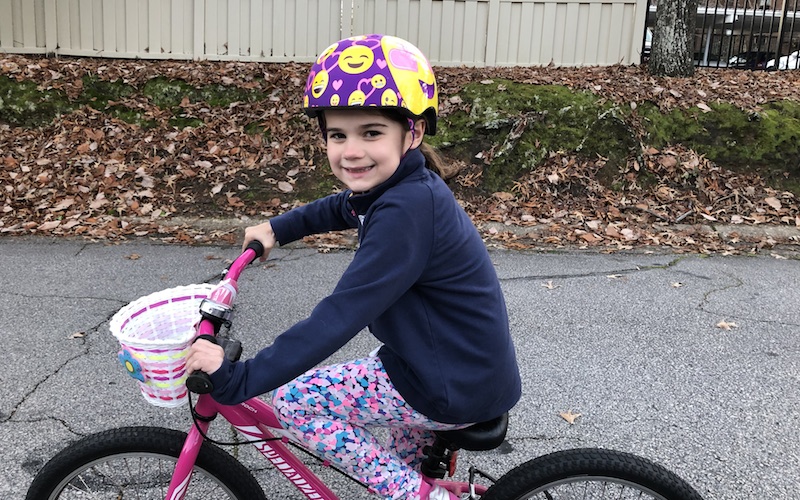 Girl in blue shirt rides pink bike on sidewalk