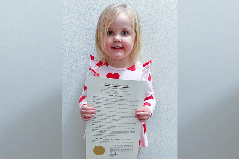Blittle blonde haired girl holds official document in front of camera