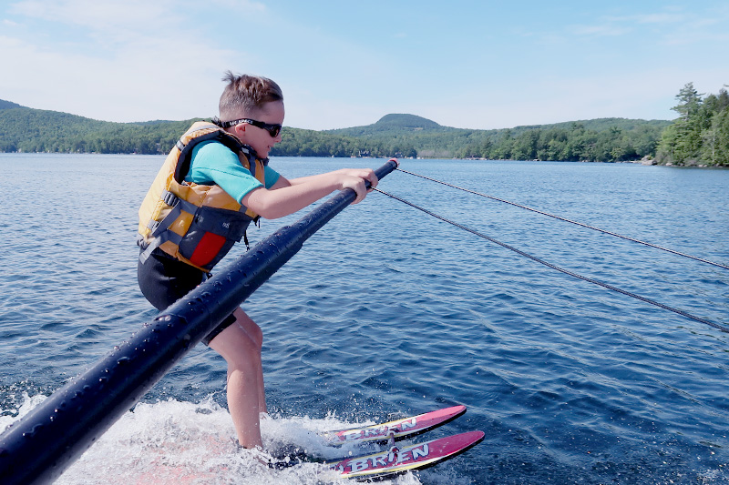 A boy on in a lifejacket waterskiing while holding onto a pole to help him balance.