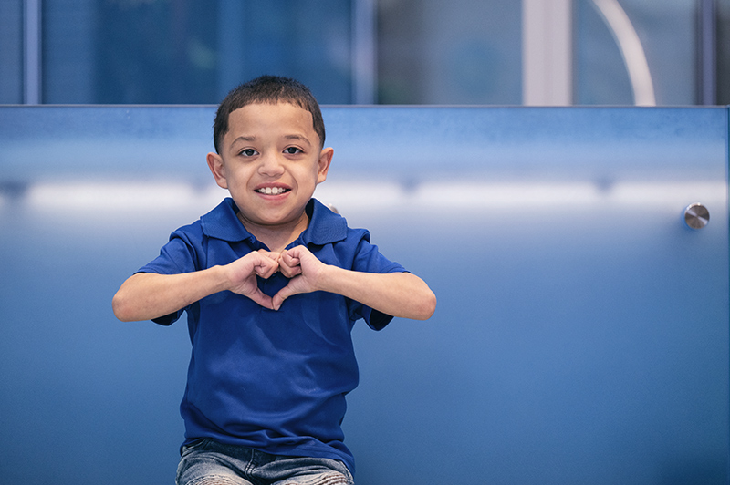 Boy wearing blue shirt holds hands in the shape of a heart