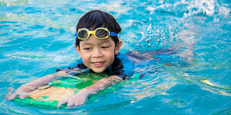 boy swimming in pool with paddle board and goggles