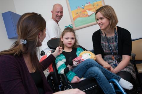 Neurology patient sitting in wheelchair accompanied by parents and clinician